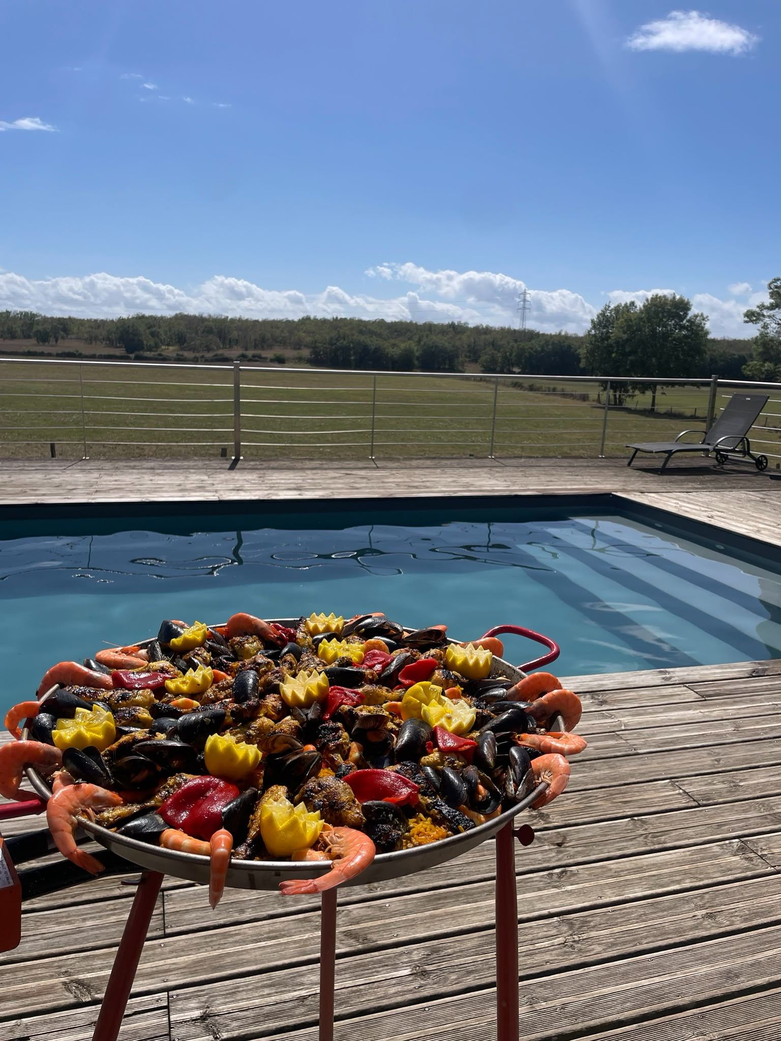Grande paella généreuse servie en extérieur au bord d'une piscine, un jour d'été près de Toulouse
